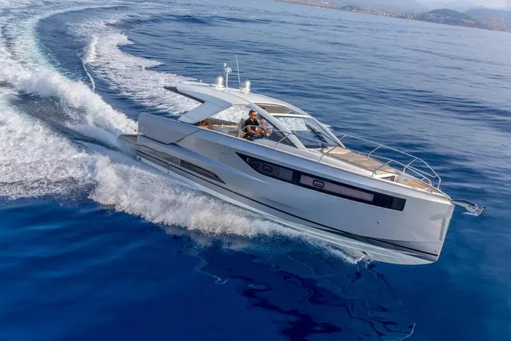 Jeanneau DB 43 IB: under way at speed on blue water, man at the helm, hull side windows and bow rail visible