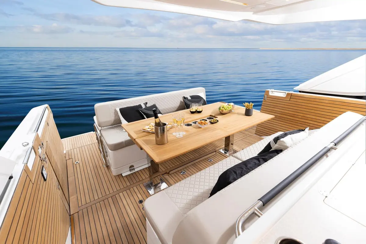 Jeanneau DB 43 OB: aft cockpit with teak table, white cushioned bench seating and teak deck overlooking calm sea