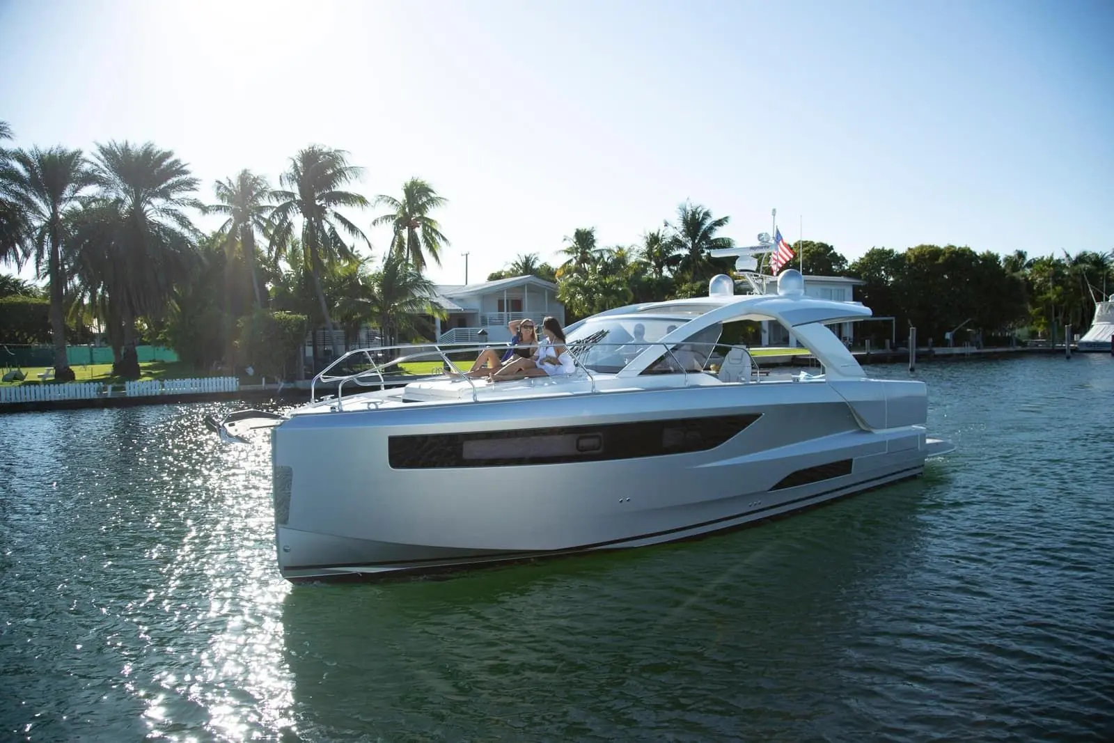 Jeanneau DB 43 OB: silver hull under way along a palm-lined canal, two people relaxing on the foredeck sunpad