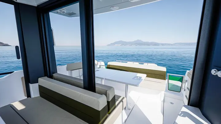 Jeanneau EX 34 Cabin: view from the cabin out to the aft cockpit, with cushioned bench seating, white table and open sea beyond