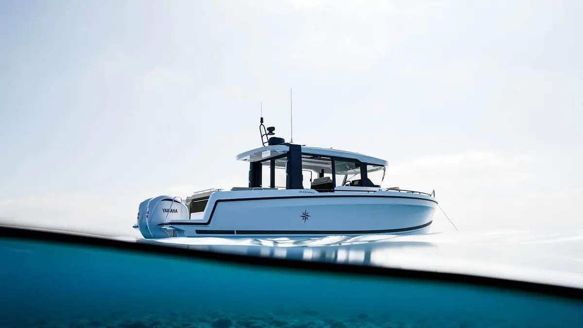 Jeanneau EX 34 Cabin: white hull with dark wheelhouse and twin outboard engines, seen from water level beside the stern