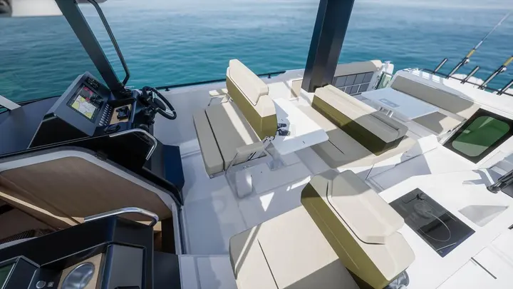 Jeanneau EX 34 Hardtop: helm and cockpit under the hardtop, with dashboard screen, steering wheel, beige seating and folding table
