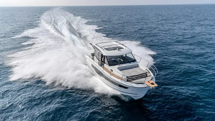 Jeanneau Merry Fisher 1095 Coupe SERIE2: aerial view from ahead of the boat at speed, foredeck sunpad and wide curving wake
