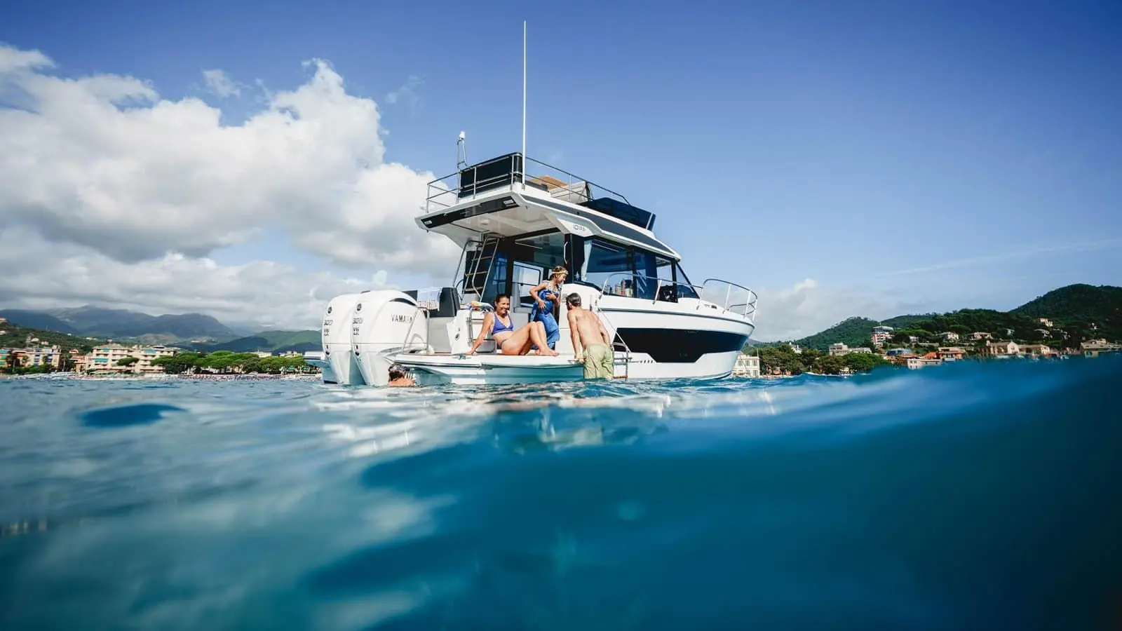 Jeanneau Merry Fisher 1095 Fly SERIE2: stern view at anchor with twin outboard engines, people relaxing on the bathing platform and flybridge above