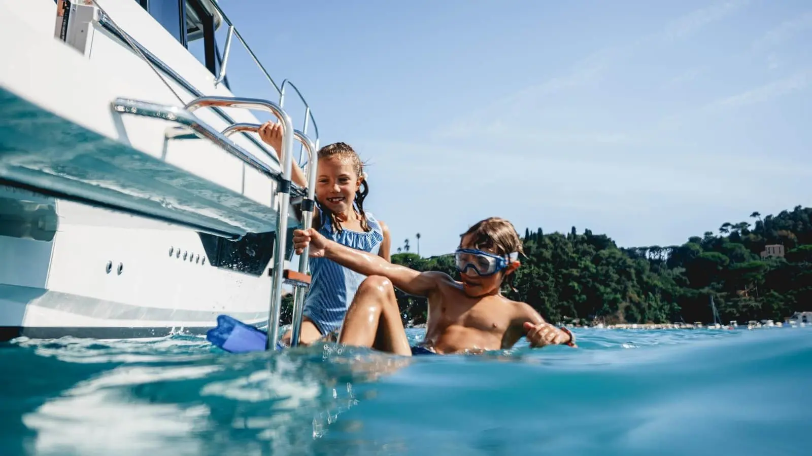 Jeanneau Merry Fisher 1095 Fly SERIE2: two children in the water beside the stern, holding the stainless steel bathing ladder, one wearing goggles