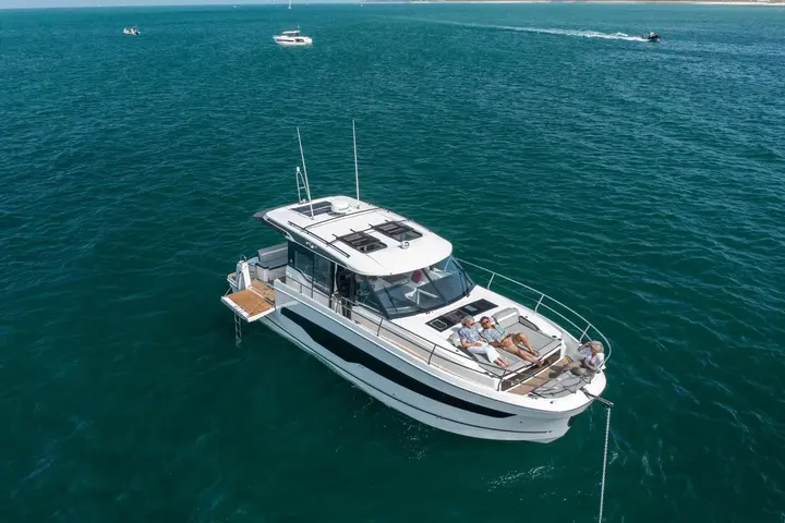 Jeanneau Merry Fisher 1295 Coupe: aerial view at anchor with three people relaxing on the foredeck sunpad and a fold-down side terrace