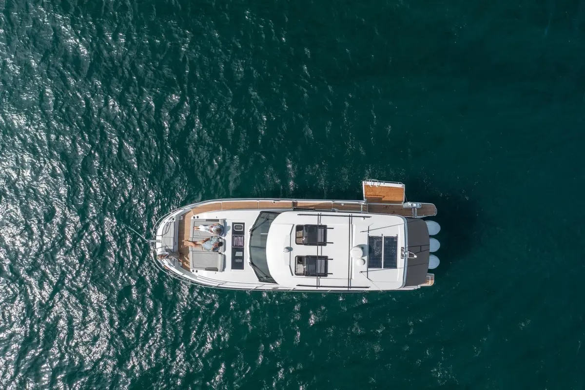 Jeanneau Merry Fisher 1295 Coupe: overhead view of the white motorboat at anchor, with people on the foredeck sunpad and three outboard engines