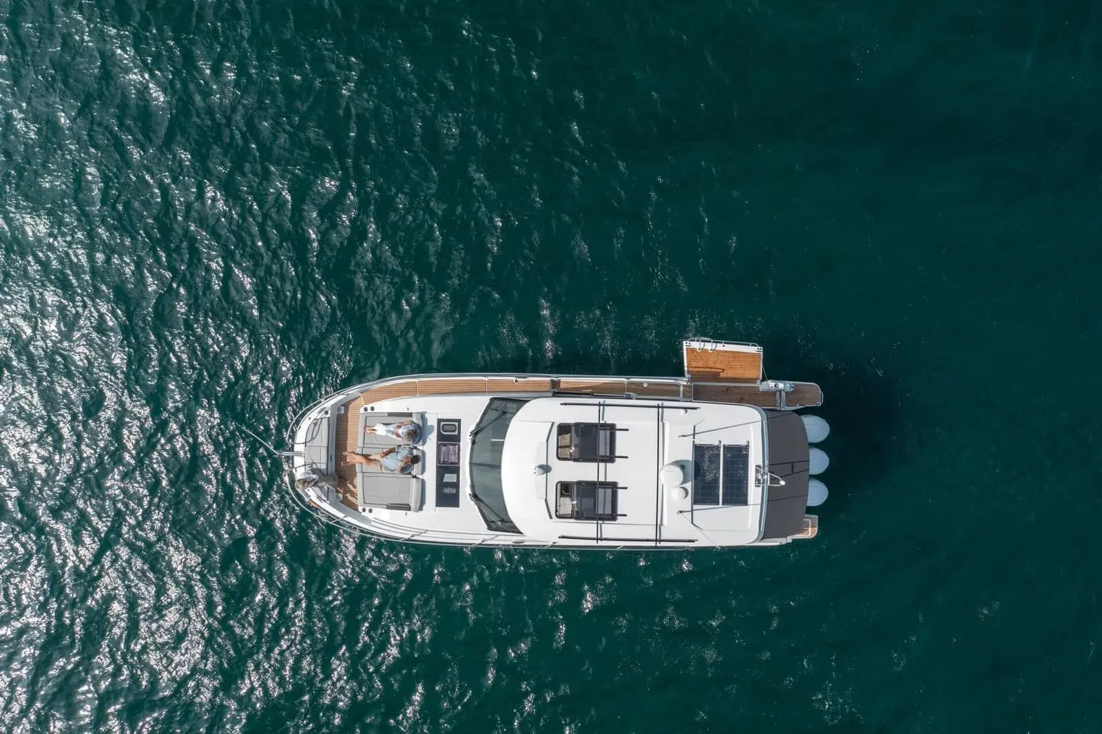 Jeanneau Merry Fisher 1295 Coupe: overhead view of the white motorboat at anchor, with people on the foredeck sunpad and three outboard engines