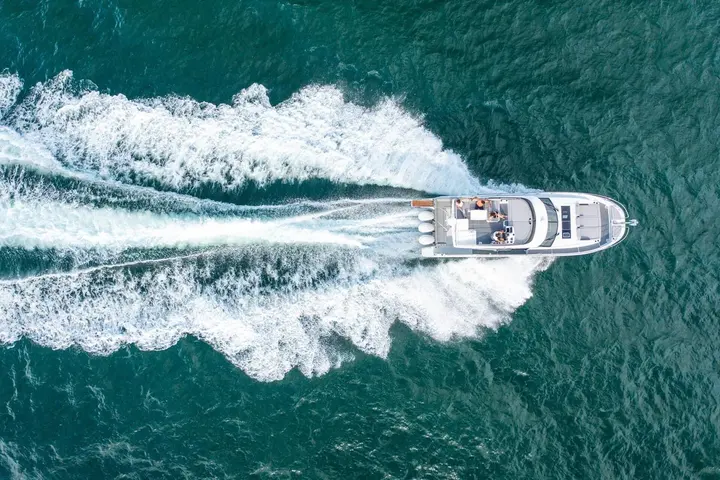 Jeanneau Merry Fisher 1295 Fly: overhead view of the boat cruising on green water, showing flybridge, foredeck and wide foaming wake