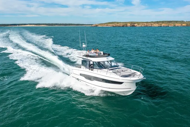 Jeanneau Merry Fisher 1295 Fly: boat under way near a rocky coastline with passengers seated on the flybridge and sunpad on the foredeck