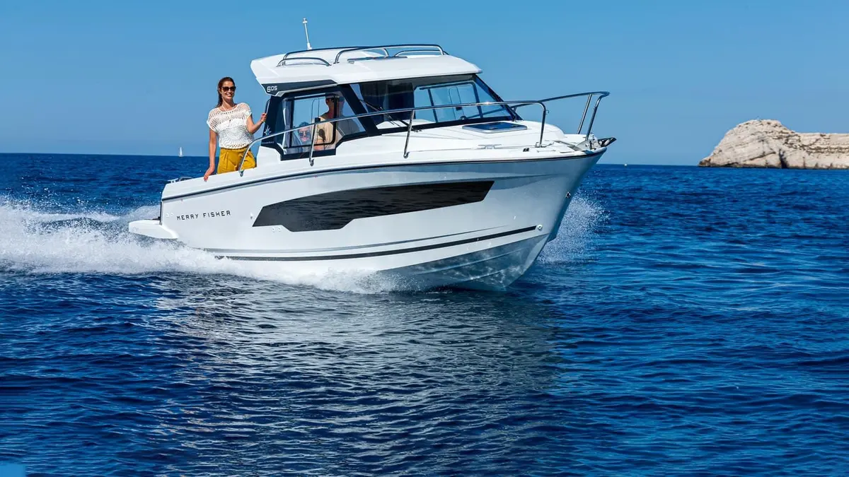 Jeanneau Merry Fisher 605: white cabin motorboat underway at speed on blue sea, woman standing at the side deck