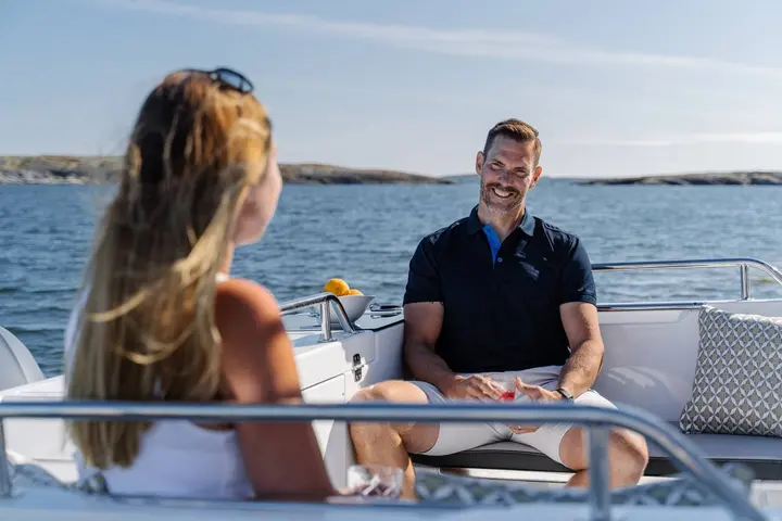 Jeanneau Merry Fisher 695 Sport: cockpit seating with a man smiling on a bench, a woman facing him, calm sea behind