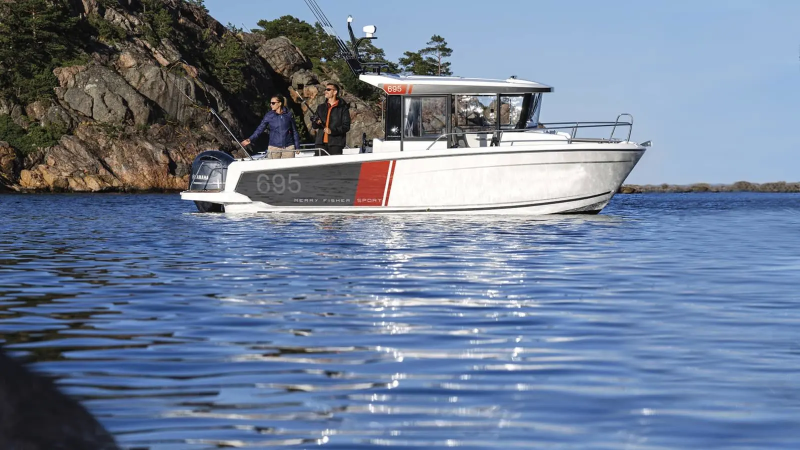 Jeanneau Merry Fisher 695 Sport: white boat with enclosed wheelhouse and outboard engine cruising near rocky shore, two people fishing from the cockpit