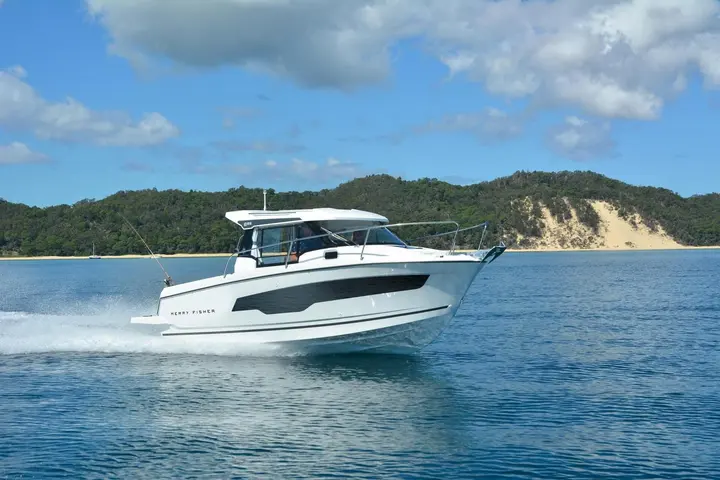 Jeanneau Merry Fisher 695: side view of the boat under way, white hull with dark window band, green hills behind