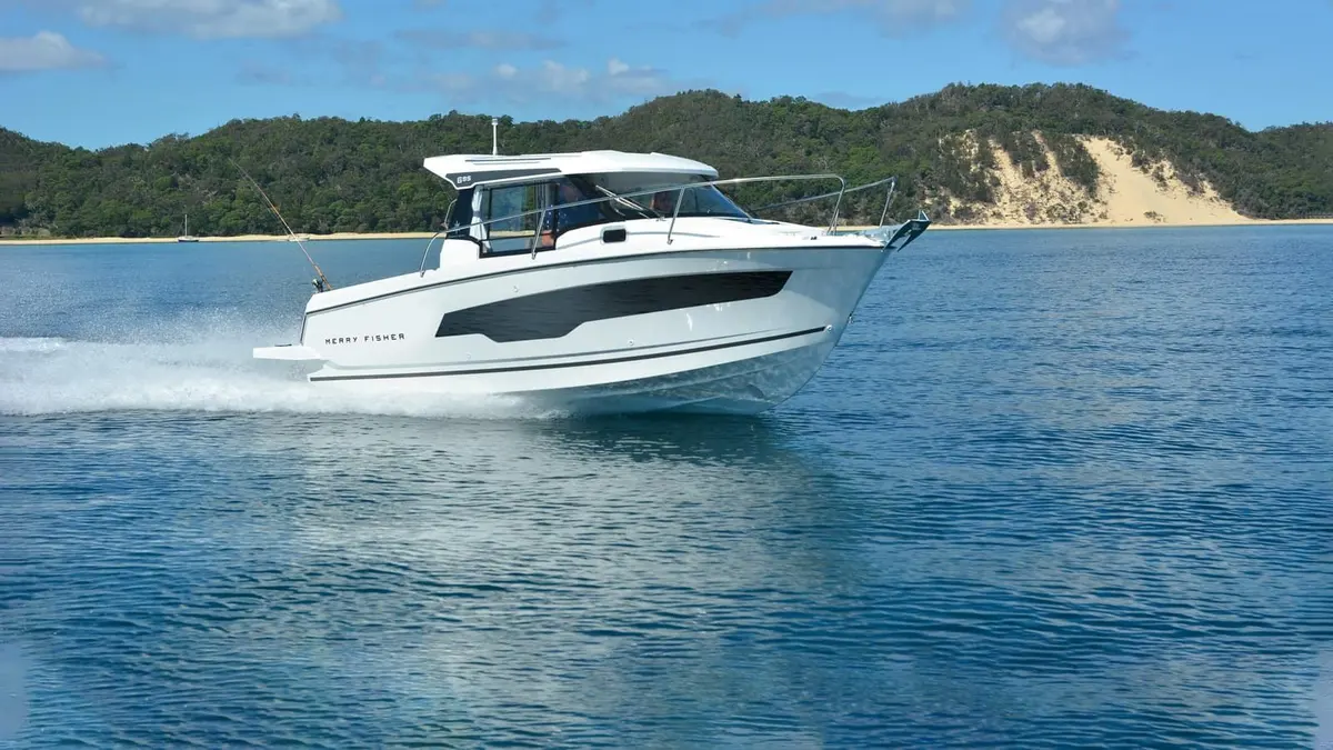 Jeanneau Merry Fisher 695: white motorboat with enclosed wheelhouse under way at speed, wooded headland and sand dune behind