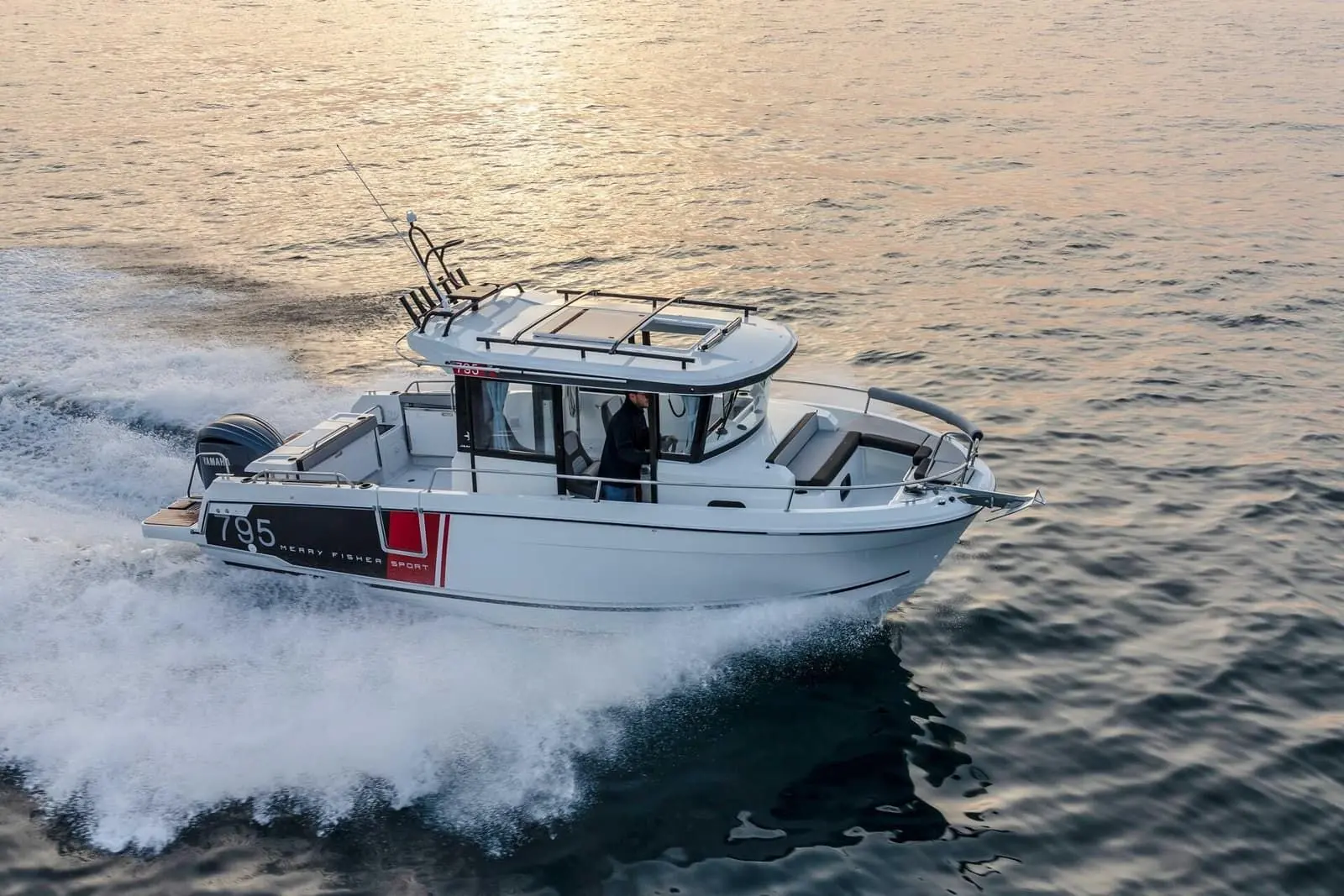 Jeanneau Merry Fisher 795 Sport: aerial view underway on calm evening water, showing wheelhouse, roof rack, rod holders and bow seating
