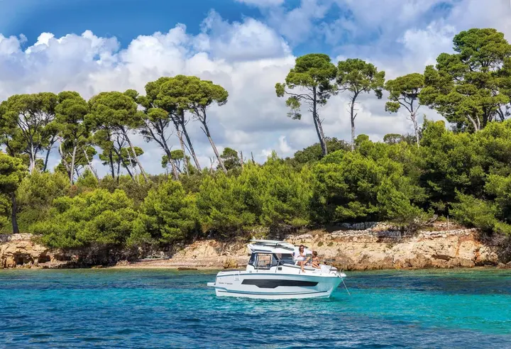 Jeanneau Merry Fisher 795: boat at anchor off a rocky wooded shore with pine trees and clear blue water
