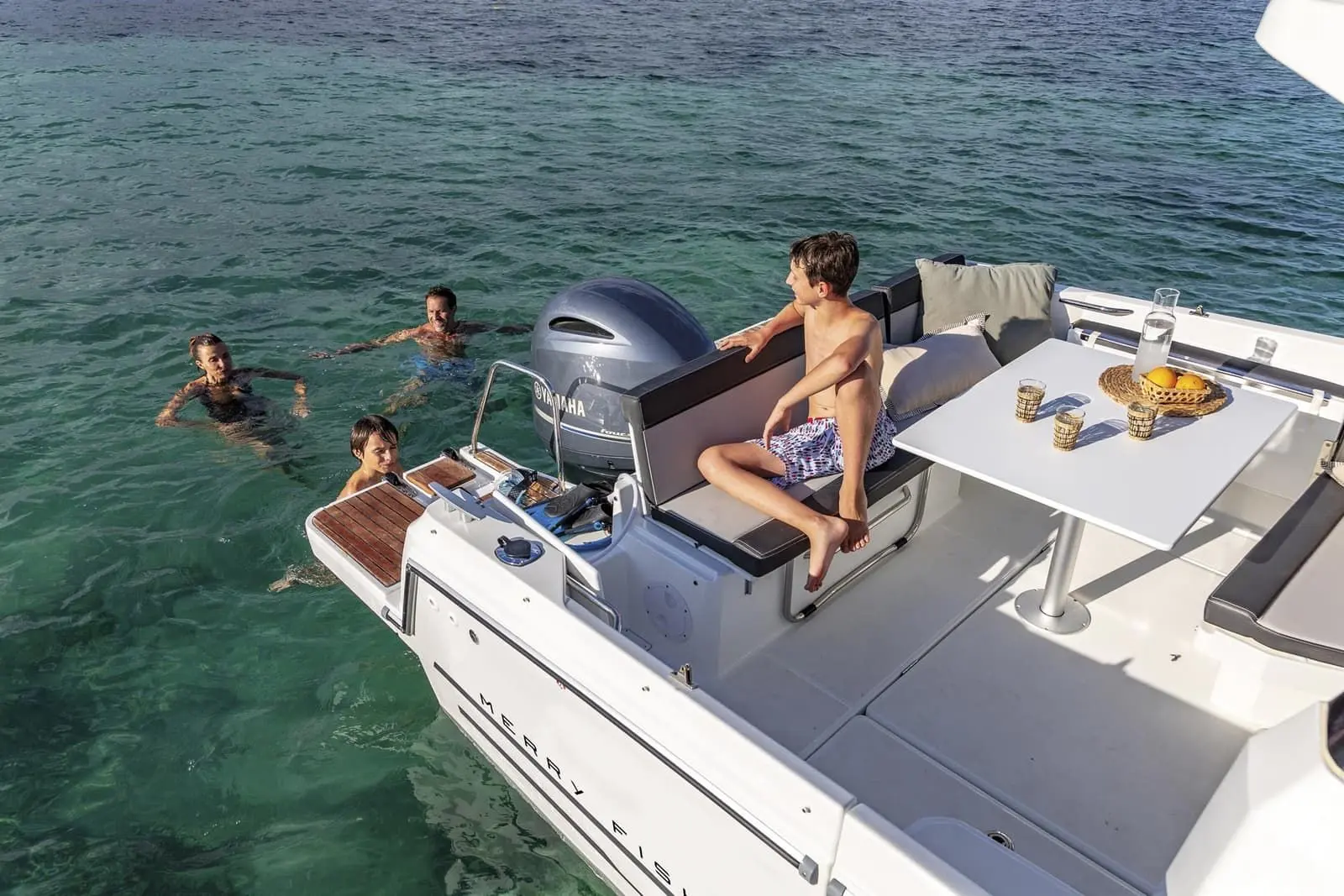 Jeanneau Merry Fisher 795: cockpit seating and table seen from above, outboard engine and bathing platforms, family swimming astern