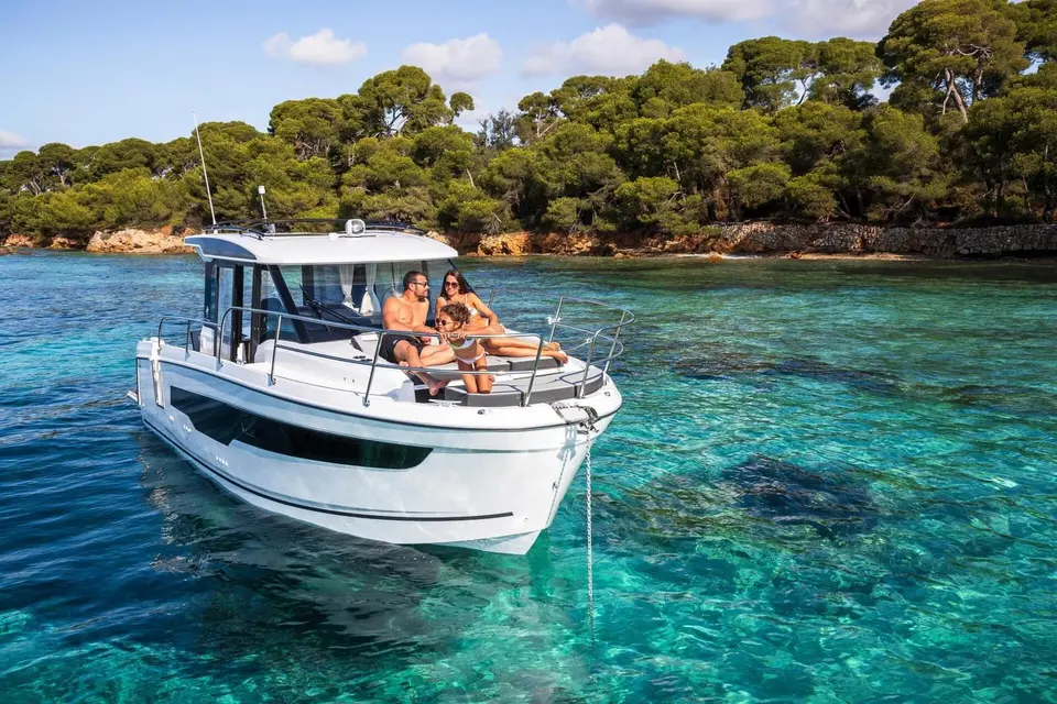 Jeanneau Merry Fisher 895 Serie 2: bow view at anchor near a wooded shore, three people seated on the foredeck sun lounger
