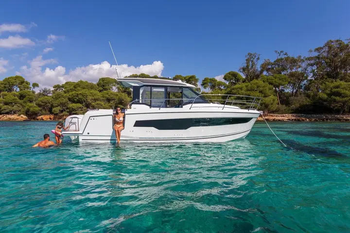 Jeanneau Merry Fisher 895 Serie 2: white motor boat at anchor in clear turquoise water, woman on side boarding steps, swimmers near stern