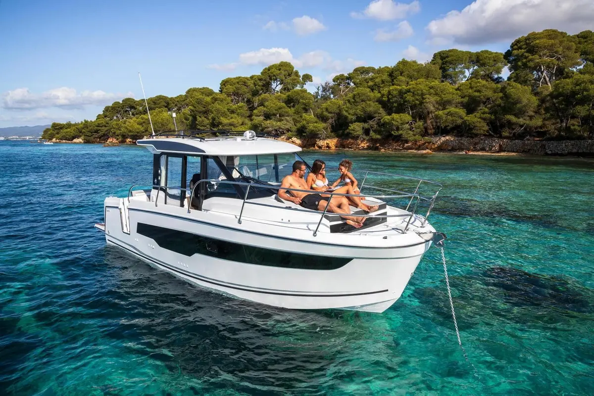 Jeanneau Merry Fisher 895 Serie 2: white wheelhouse motorboat at anchor in clear turquoise water, three people relaxing on the foredeck seating
