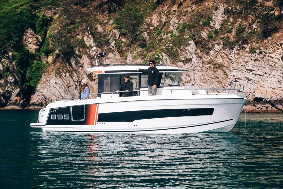 Jeanneau Merry Fisher 895 Sport Série 2: side view at anchor below rocky cliffs, three people on deck and at the wheelhouse door