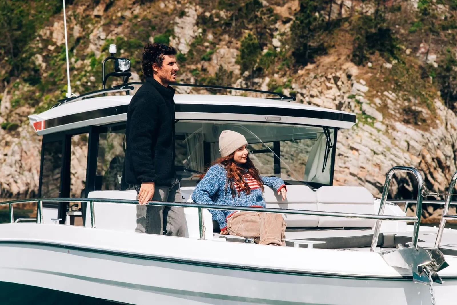 Jeanneau Merry Fisher 895 Sport Série 2: two people at the forward wheelhouse area, one standing by the side rail, one seated