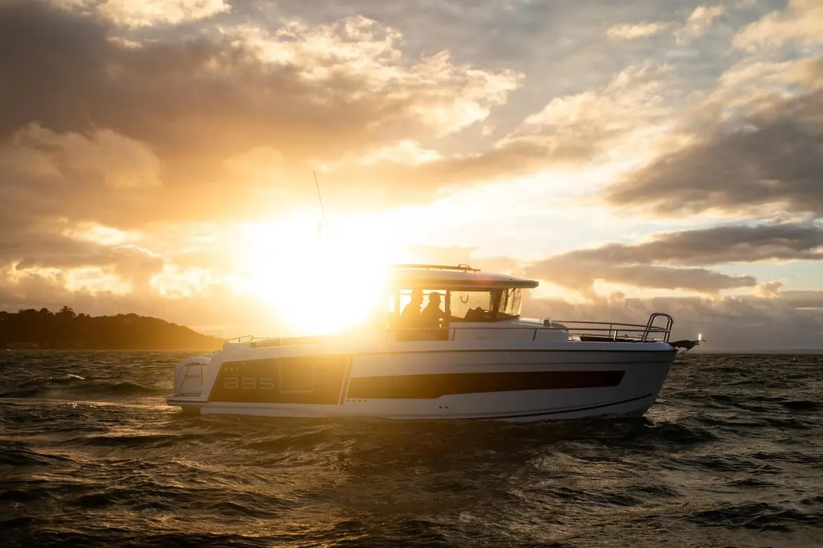 Jeanneau Merry Fisher 895 Sport Série 2: boat underway at sunset, silhouetted against a bright low sun and cloudy sky, people in wheelhouse
