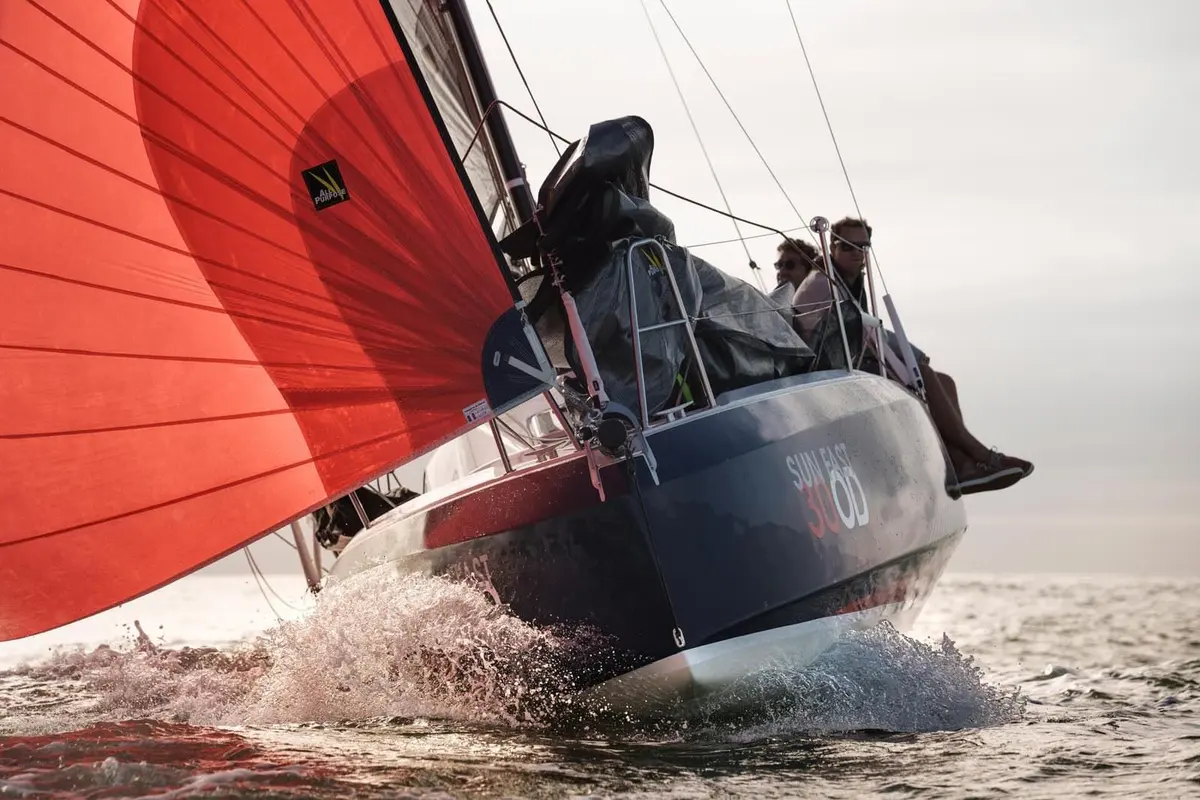 Jeanneau Sun Fast 30 OD: close low view of the bow under red spinnaker, crew seated on the rail above spray