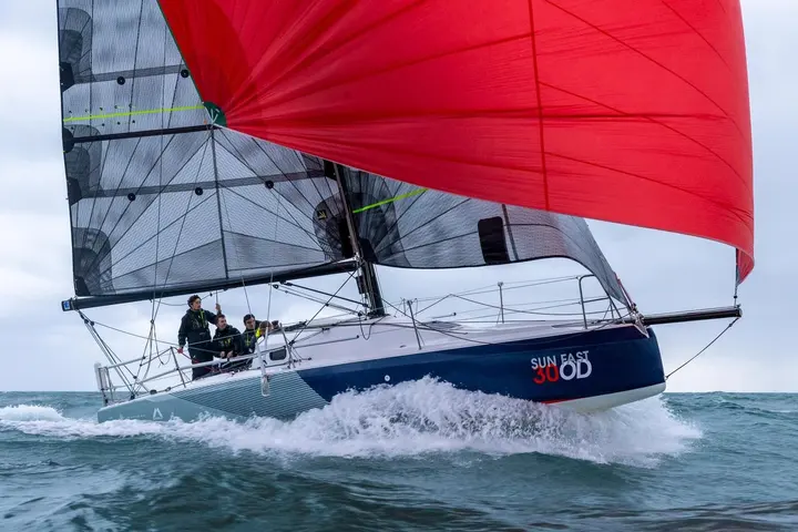 Jeanneau Sun Fast 30 OD: under sail with red spinnaker and dark mainsail, crew in the cockpit, bow throwing spray