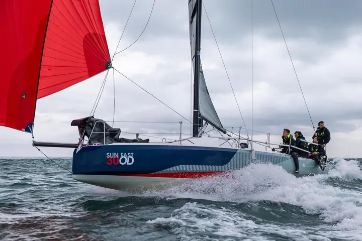 Jeanneau Sun Fast 30 OD: side view under red spinnaker in choppy water, four crew hiking out on the side