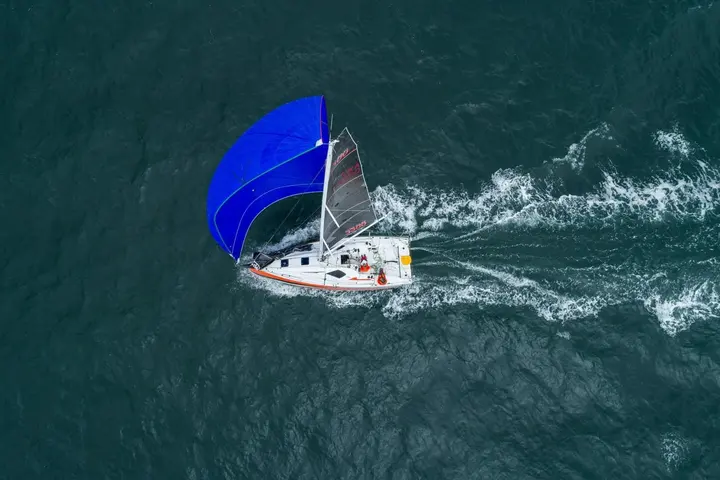 Jeanneau Sun Fast 3300: aerial view under blue spinnaker on dark green water, leaving a white wake