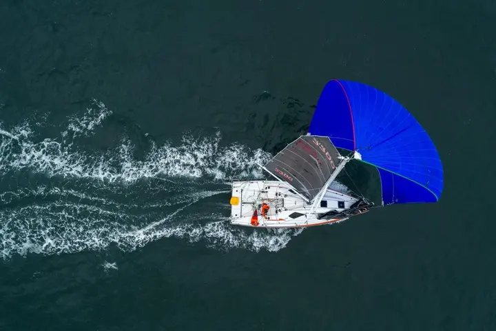 Jeanneau Sun Fast 3300: aerial view of the boat under blue spinnaker and dark mainsail, leaving a white wake