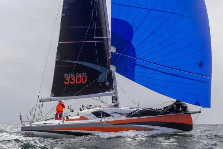 Jeanneau Sun Fast 3300: under sail with large blue spinnaker and black mainsail, one crew member in the cockpit