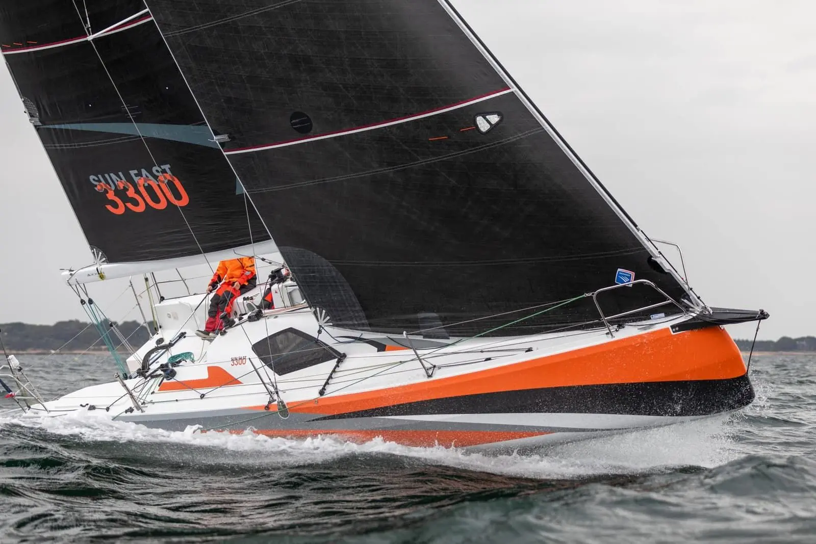 Jeanneau Sun Fast 3300: under sail upwind, white hull with orange and black stripes, black sails, crew at the stern