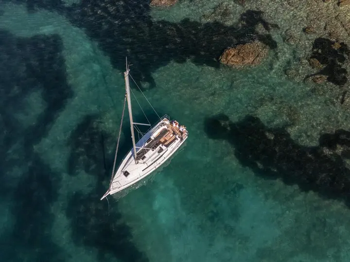 Jeanneau Sun Odyssey 350: overhead view at anchor over clear water and rocks, people relaxing in the cockpit