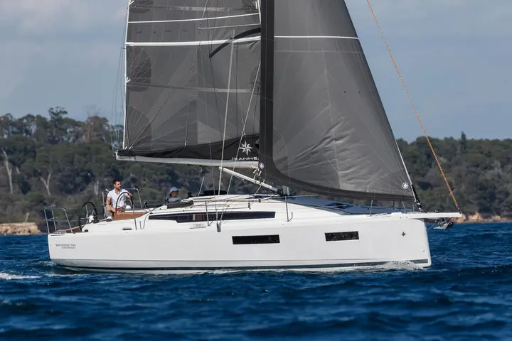 Jeanneau Sun Odyssey 350: side view under sail with grey mainsail and jib, two people at the twin wheels