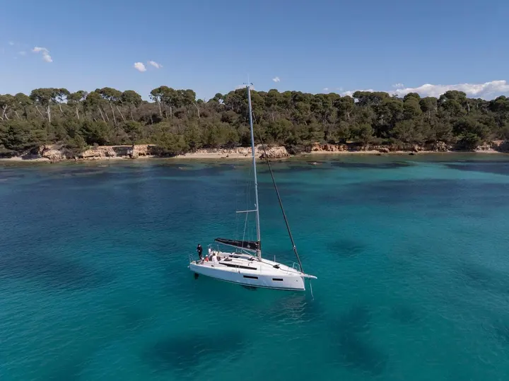 Jeanneau Sun Odyssey 350: white sailing yacht at anchor in turquoise water off a pine-covered rocky shore