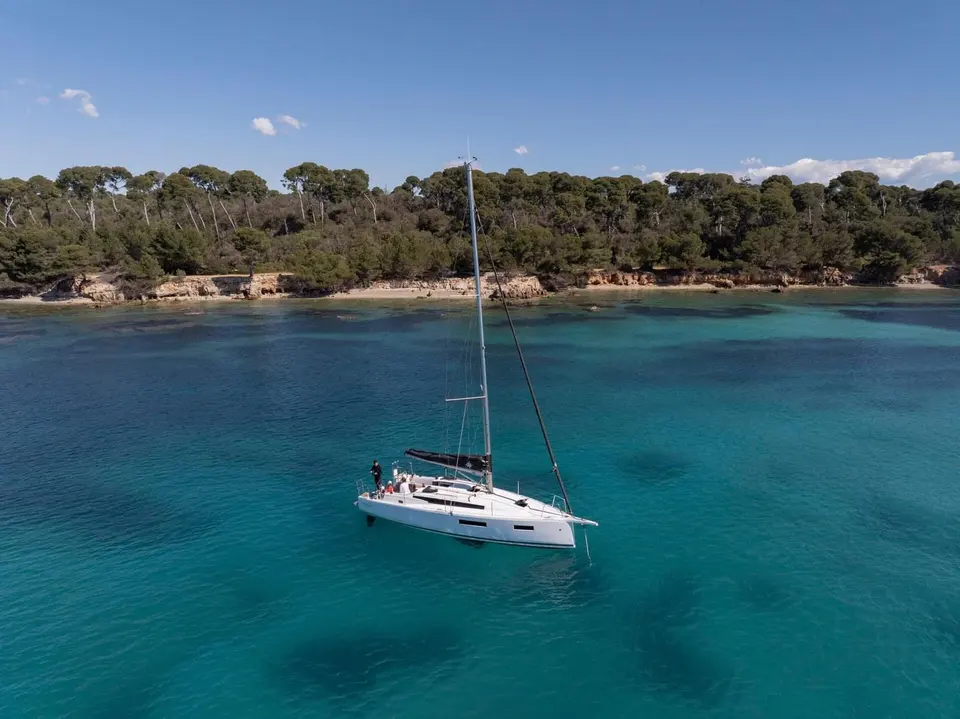 Jeanneau Sun Odyssey 350: white sailing yacht at anchor in turquoise water off a pine-covered rocky shore