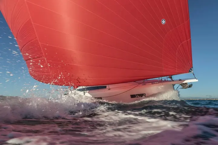 Jeanneau Sun Odyssey 380: low view of the bow slicing through spray beneath a billowing red gennaker
