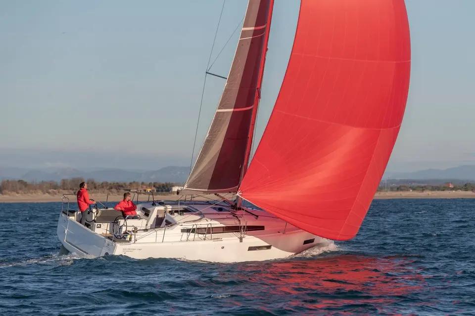 Jeanneau Sun Odyssey 380: under sail on choppy blue water with a large red gennaker and mainsail, coastline behind