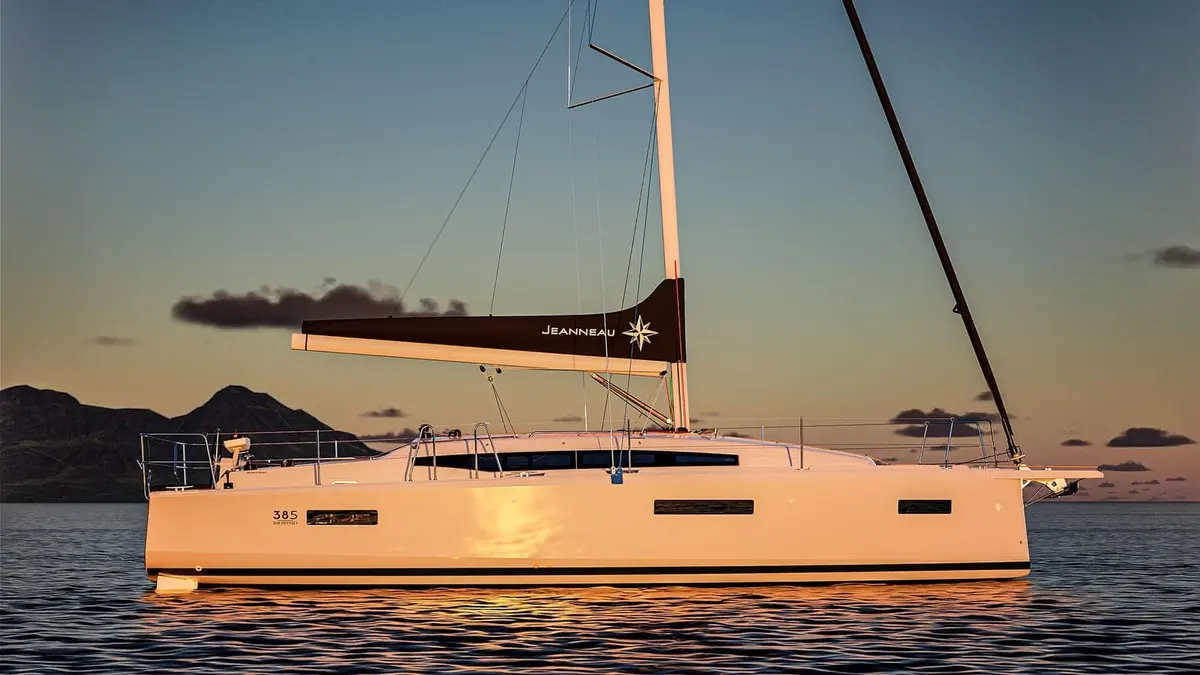 Jeanneau Sun Odyssey 385: white sailing yacht at anchor in profile at sunset, mainsail furled in a dark boom cover