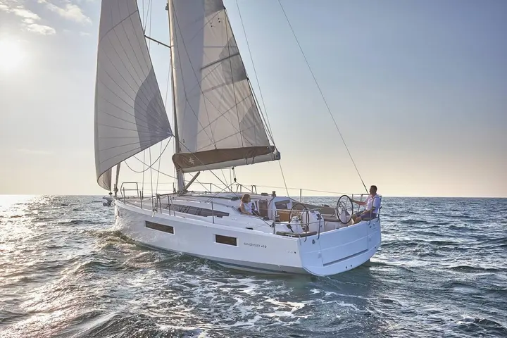 Jeanneau Sun Odyssey 410: under sail in low sunlight, mainsail and headsail set, two people seated in the cockpit