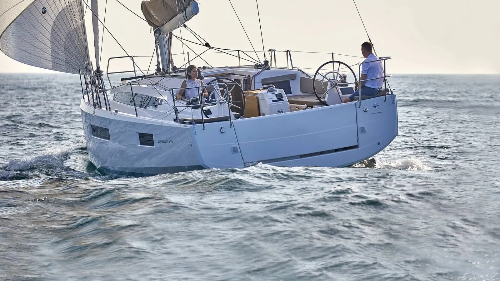 Jeanneau Sun Odyssey 410: stern quarter view under sail, two people at the twin wheels in the cockpit