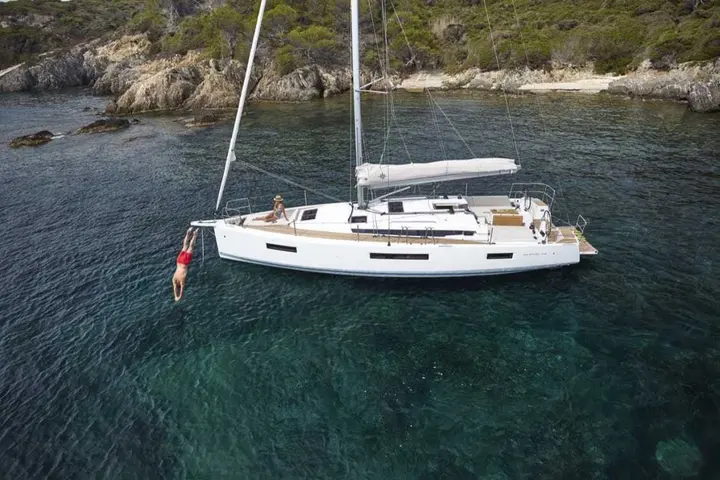 Jeanneau Sun Odyssey 440: at anchor in a rocky cove, mainsail stowed, swimmer diving from the bow