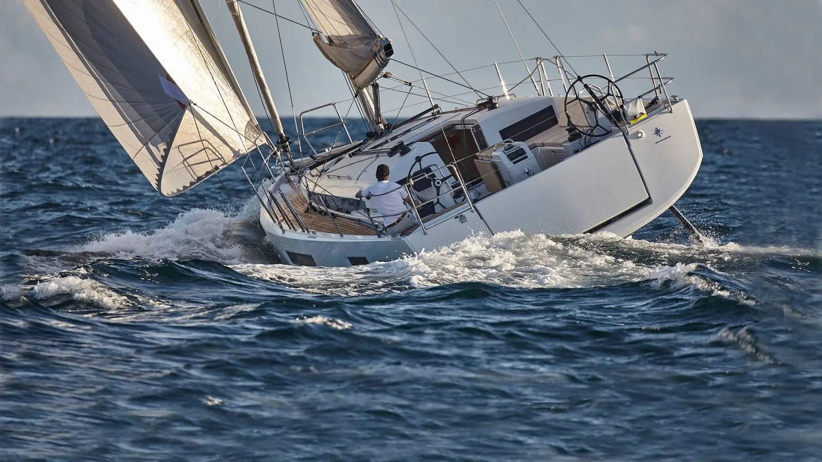Jeanneau Sun Odyssey 440: heeled hard under sail through choppy water, helmsman seated at one of the twin wheels