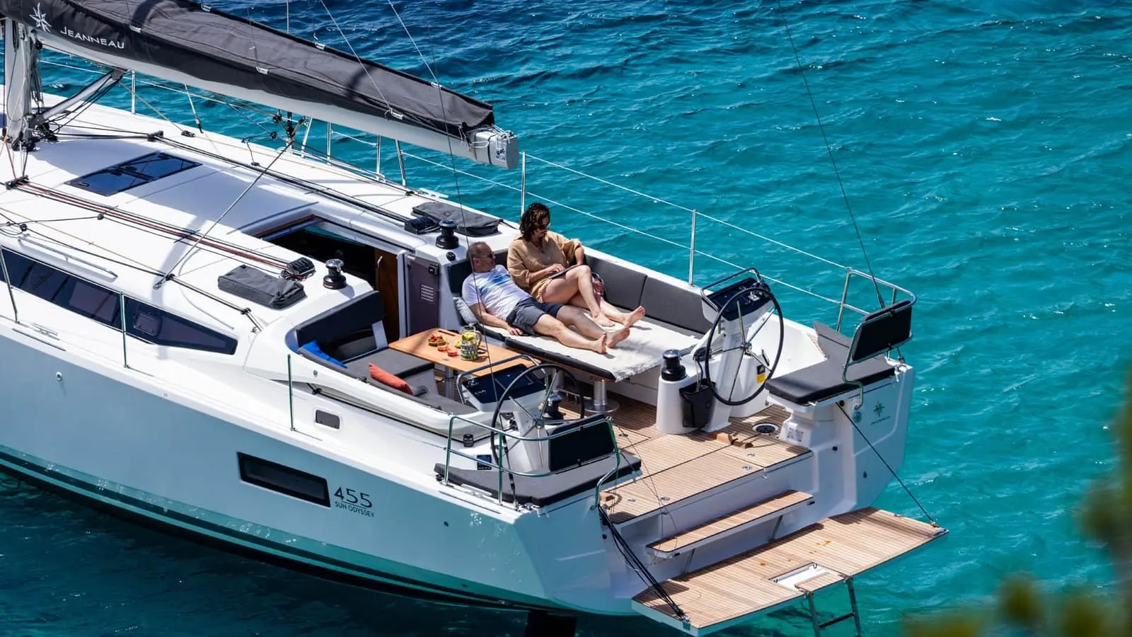 Jeanneau Sun Odyssey 455: aft cockpit with twin wheels, teak bathing platform lowered and a couple lounging on cushions