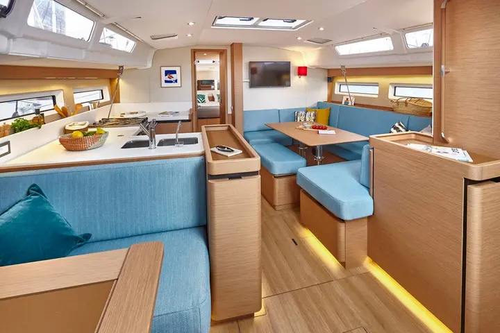 Jeanneau Sun Odyssey 490: saloon with light wood joinery, blue upholstered seating, galley with double sink, and dining table