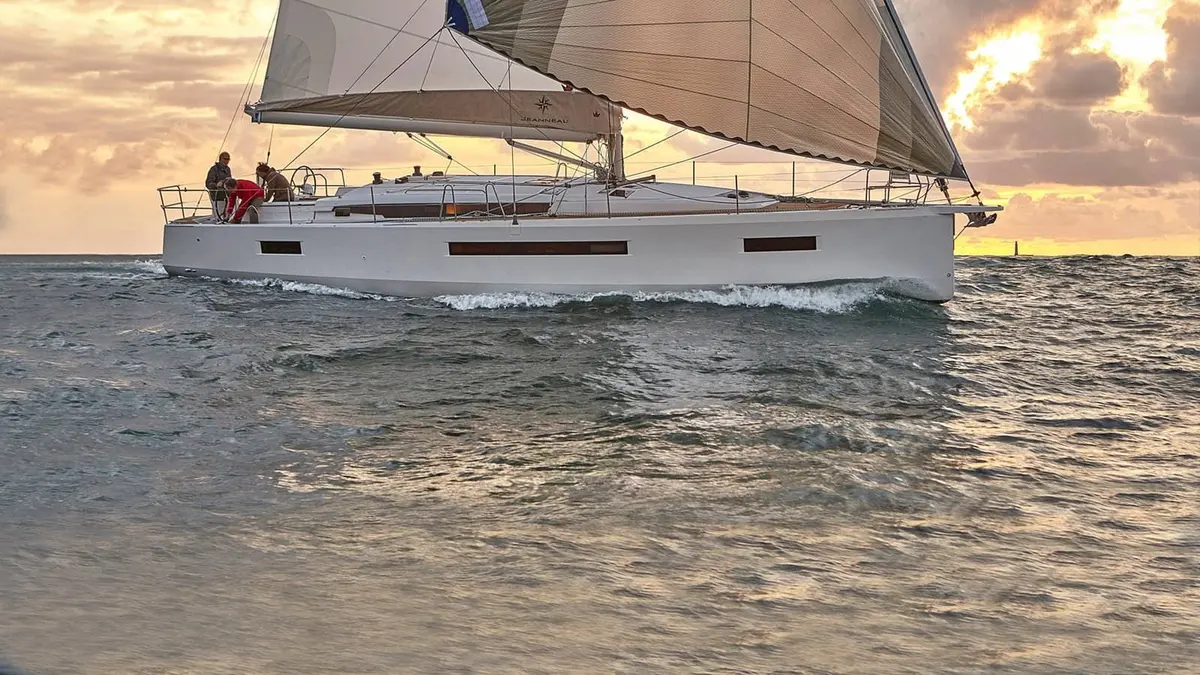Jeanneau Sun Odyssey 490: white-hulled yacht under sail at sunset, crew in the cockpit, waves breaking along the hull