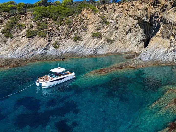 Jeanneau TH33: at anchor in a clear turquoise cove beneath striped rock cliffs, guests on the bow